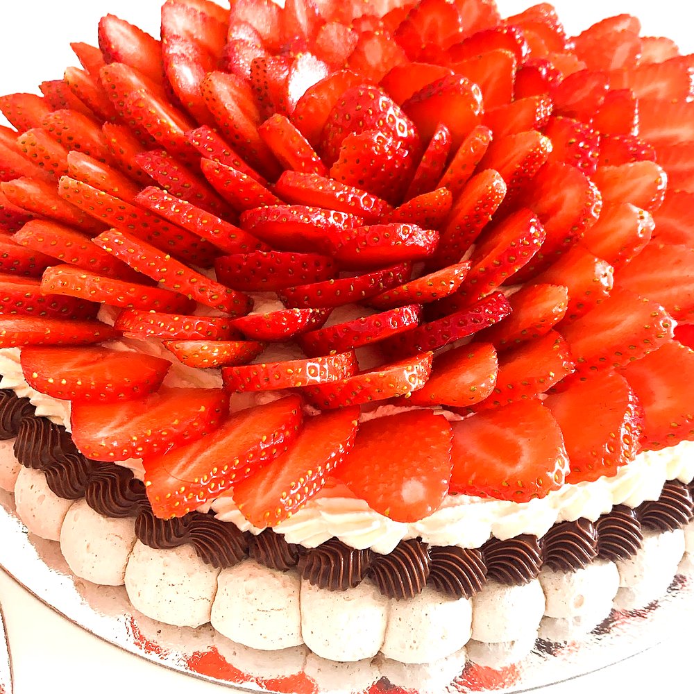 A Cakish strawberry pavlova seen from above, with a floral strawberry arrangement.